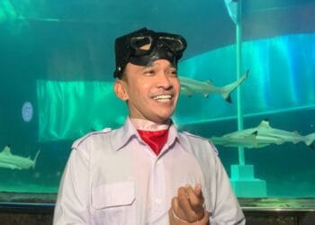 Ruben Onsu mengenakan seragam Paskibraka lengkap saat beraksi di dasar akuarium hiu, tampak fokus dalam kondisi air. © Grid.ID / Ragillita Desyaningrum