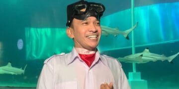 Ruben Onsu mengenakan seragam Paskibraka lengkap saat beraksi di dasar akuarium hiu, tampak fokus dalam kondisi air. © Grid.ID / Ragillita Desyaningrum