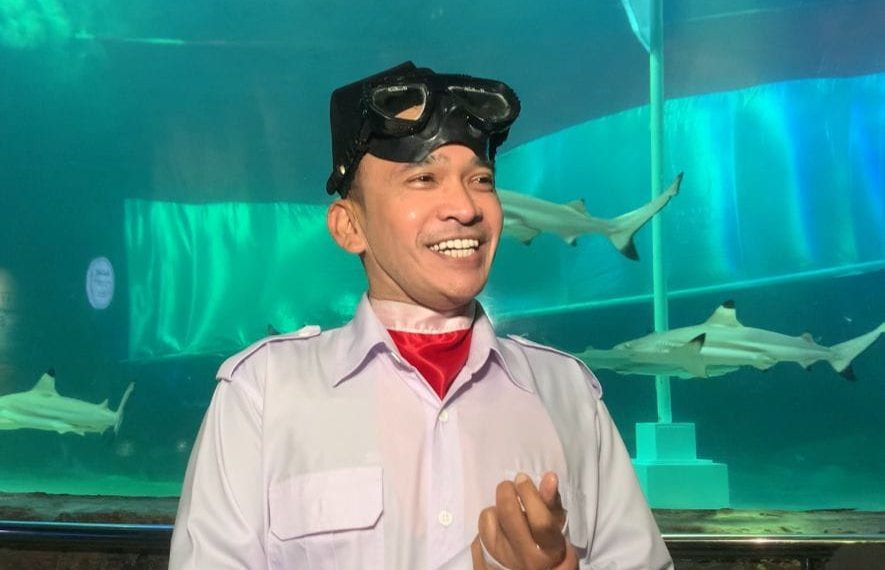 Ruben Onsu mengenakan seragam Paskibraka lengkap saat beraksi di dasar akuarium hiu, tampak fokus dalam kondisi air. © Grid.ID / Ragillita Desyaningrum