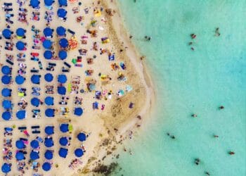 Suasana pantai yang sangat ramai—tumpah ruah pengunjung di sepanjang pasir dan tepian laut, menggambarkan betapa padatnya beberapa pantai wisata favorit dunia. Sumber: Dreamstime