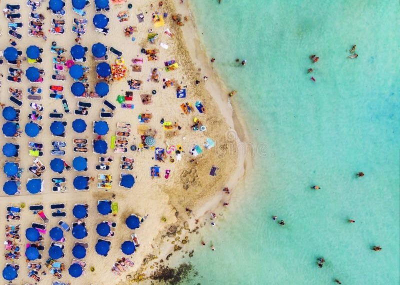 Suasana pantai yang sangat ramai—tumpah ruah pengunjung di sepanjang pasir dan tepian laut, menggambarkan betapa padatnya beberapa pantai wisata favorit dunia. Sumber: Dreamstime