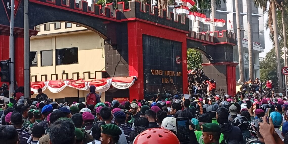 Visual memperlihatkan massa pengemudi ojol tengah melakukan aksi di depan Mako Brimob Kwitang, diselingi dengan penggunaan gas air mata oleh aparat. (Sumber: Okezone)