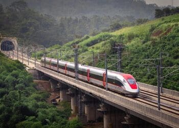 Kereta cepat Whoosh melaju di atas rel dengan latar hijau, menggambarkan momen sesaat sebelum gangguan terjadi karena layang-layang. (Sumber: detikFinance)