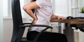 Ilustrasi seseorang duduk membungkuk di depan laptop—contoh posisi yang umum tapi bisa menyebabkan sakit leher dan punggung. (Sumber: Alodokter)