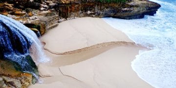 Tebing karang yang membingkai pantai dengan ombak biru jernih dan pasir lembut—suasana alami sekaligus menyejukkan. (Sumber: Indonesiakaya.com)