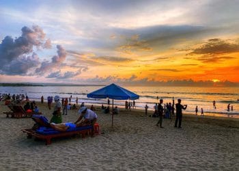 Pantai Kuta saat senja—langit jingga berpadu sempurna dengan ombak tenang dan pasir putih yang memesona. (Sumber: Tripcetera.com)